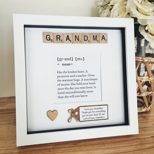 May include: A white picture frame with a black mount and a white background. The frame contains a definition of the word "Grandma" written in black text. The definition is "[gr-and] [mA] noun- Has the kindest heart. A protector and a teacher. Gives the warmest hugs. A true keeper of secrets. Has held your hand since the day you were born. Is loved unconditionally, more than she will ever know." There is a small wooden heart and a brown tag with the text "I love you Grandma, Thank you for everything you've ever done for me. Lots of love, Hannah x" in black text.