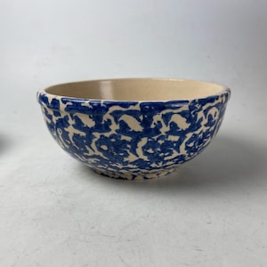 May include: A ceramic bowl with a cream-colored interior and a blue patterned exterior. The blue pattern is a repeating design of abstract shapes. The bowl has a rounded shape and a slightly flared rim. The bowl is likely used for serving food.