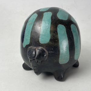 May include: A ceramic sculpture of a round, stylized animal with a black body and turquoise stripes. The sculpture has small legs and a detailed face with large eyes. The piece is likely handmade and decorative.