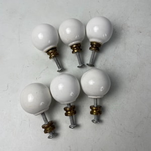 May include: Six white ceramic cabinet knobs with brass accents and silver screws. These round knobs are ideal for adding a touch of elegance to furniture or cabinetry. The knobs are approximately 1.5 inches in diameter.