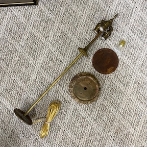 May include: Disassembled vintage floor lamp with a brass pole, three-bulb socket, and a round, rusty base. The lamp includes a decorative base, a small round base, and a yellow electrical cord. The lamp is designed to be assembled.