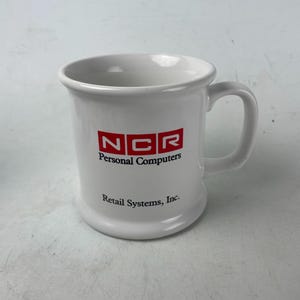 May include: White ceramic mug with a rounded base and a handle. The mug features the red and white "NCR Personal Computers" logo and the text "Retail Systems, Inc."
