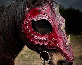 May include: A red leather horse mask with a dragon-like design, featuring decorative studs and horn-like protrusions. The mask is adorned with intricate patterns and is attached to a bridle. The horse has dark brown fur.