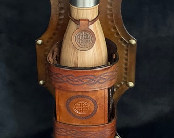 May include: A brown leather bottle holder with a Celtic knot design. The holder is attached to a strap and has a metal buckle. A stainless steel water bottle with a wooden exterior is inside the holder.