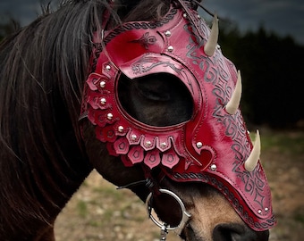 May include: A red leather horse head covering with decorative details and horns. The covering is designed to protect the horse's head and face.