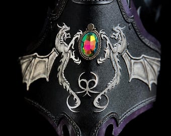 May include: A black leather bracer featuring two silver-toned dragon emblems with spread wings flanking a central oval iridescent gemstone. The piece includes decorative stitching along the edges and a logo reading FANGORN RANCH at the bottom.