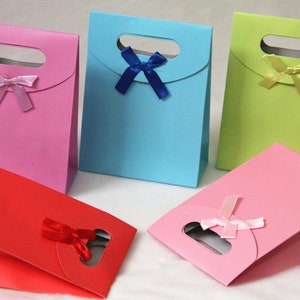 May include: Five small gift bags in different colors, each with a bow. The bags are pink, blue, green, red, and light pink. The bags have a cut-out handle and are made of paper.