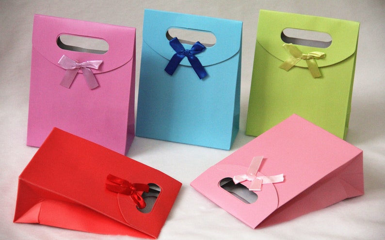 May include: Five small gift bags in different colors, each with a bow. The bags are pink, blue, green, red, and light pink. The bags have a cut-out handle and are made of paper.