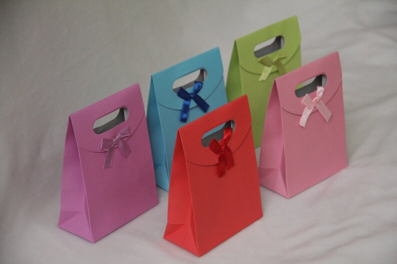 May include: Five small gift bags with different colored paper and ribbon bows. The bags are pink, red, blue, green, and light pink.