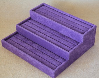 May include: A three-tiered purple velvet ring holder with multiple slots for storing rings.