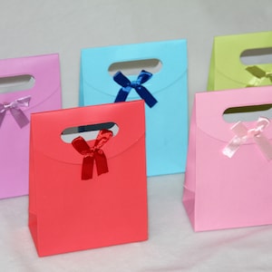 May include: Five colorful gift bags with cut-out handles and satin ribbon bows. The bags are in shades of pink, light blue, green, red, and lavender.