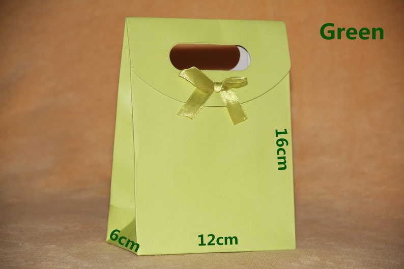 May include: A green gift bag with a yellow ribbon and a cut-out handle. The bag measures 6 inches by 12 inches by 16 inches.