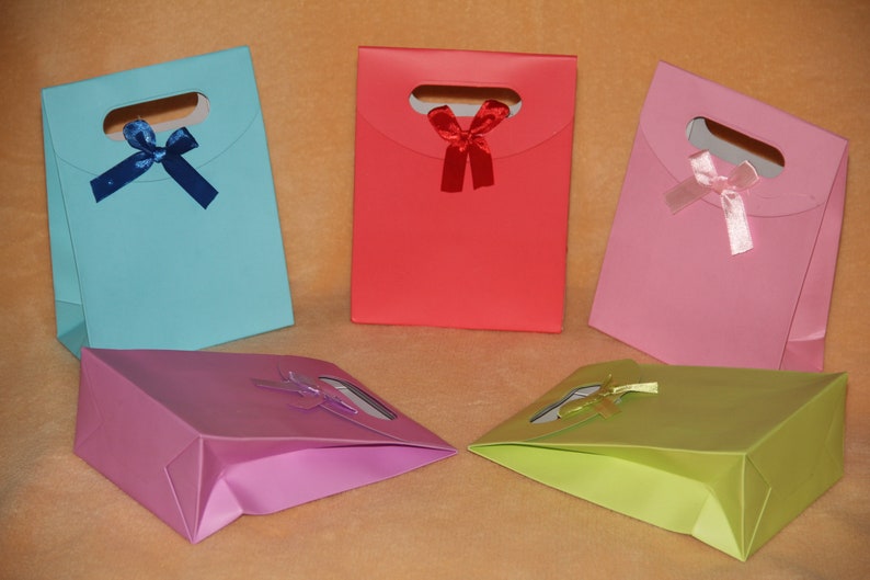 May include: Five gift bags in different colors, each with a bow. The bags are light blue, red, pink, purple, and green. The bags have a cut-out handle and are made of paper.