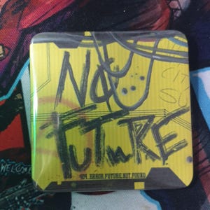 Puede incluir: Botón cuadrado con fondo amarillo y las palabras "NO FUTURE" en negro, estilo grafiti. El botón también incluye el texto "404 ERROR. FUTURE NOT FOUND". El botón está envuelto en plástico transparente.