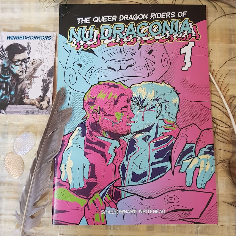 This picture contains the front cover of the comic. It depicts two men kissing, while being embraced by two dragons. The colours are very vivid going from neon pink to neon cyan. The title read'The queer dragon riders of Nu Draconia 1'