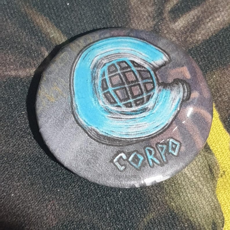 May include: A round, gray button with a blue and white graphic of a circle with a grid pattern inside. The word "CORPO" is written in blue below the graphic.