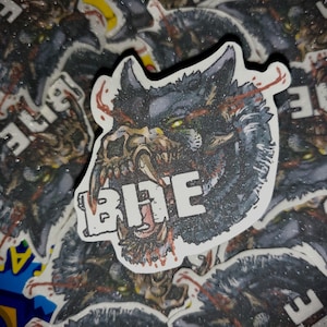 May include: A sticker featuring a detailed illustration of a wolf-like creature with a skull-like face and glowing green eyes. The word "BITE" is printed in white. The sticker has a dark, textured background.