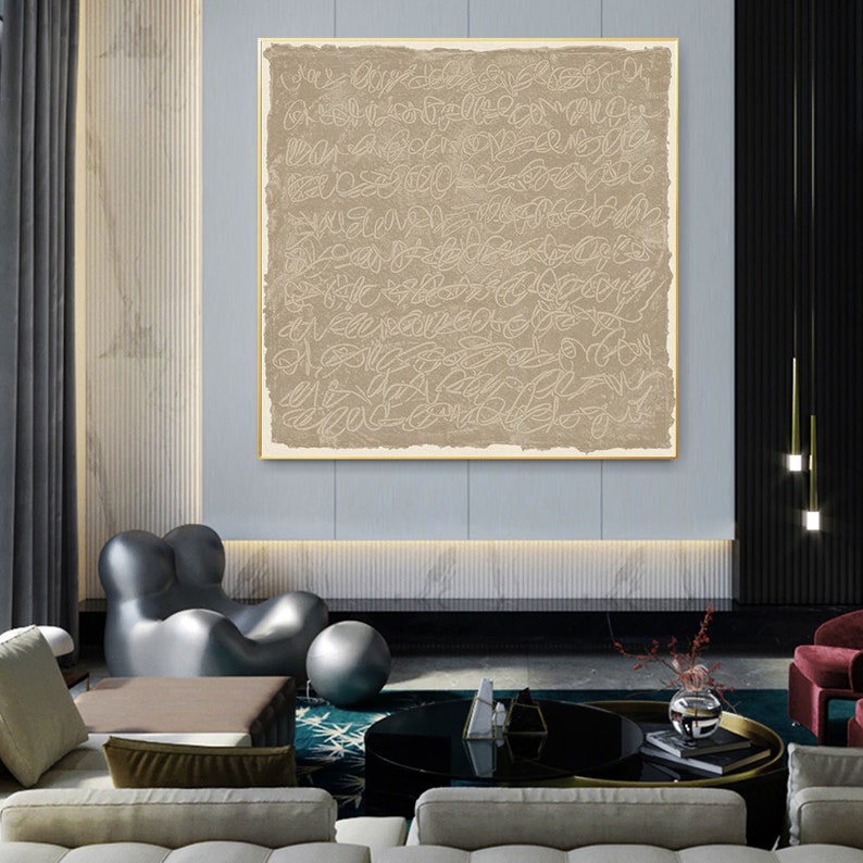 Puede incluir: Un arte de pared de lienzo beige con un dise&ntilde;o abstracto blanco. El arte est&aacute; colgado en una sala de estar moderna con un sof&aacute; gris, una mesa de caf&eacute; negra y una alfombra gris y blanca.