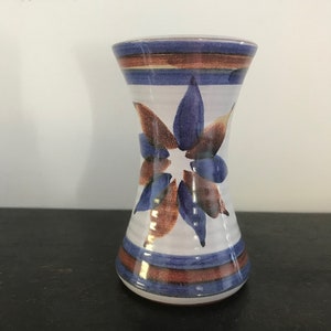 May include: A white ceramic vase with a blue and brown floral design. The vase has a narrow neck and a wide base.