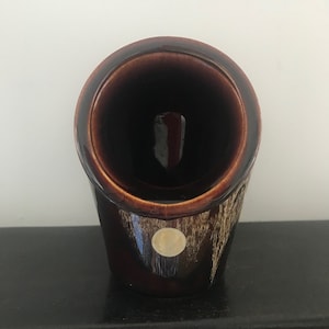 May include: A brown ceramic salt cellar with a round opening and a gold circle on the side.