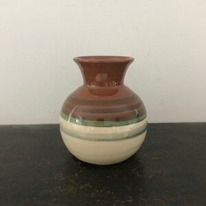 Puede incluir: Un jarrón pequeño, redondo, de cerámica marrón con un diseño de rayas blancas y verdes.