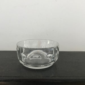 Puede incluir: Un cuenco de vidrio transparente con un diseño texturizado y ondulado. El cuenco está vacío y se encuentra sobre una superficie oscura.