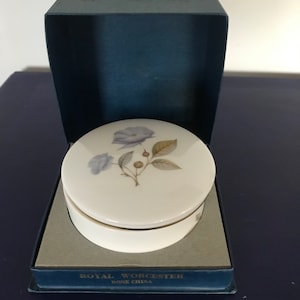 May include: A white porcelain trinket box with a blue floral design. The box is in its original blue box with gold lettering that reads "Royal Worcester Bone China".