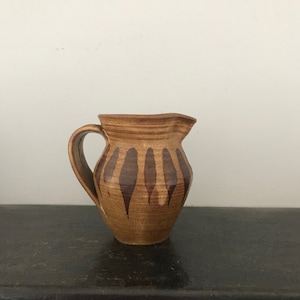 May include: A brown ceramic jug with a brown and white striped design. The jug has a handle and a spout.