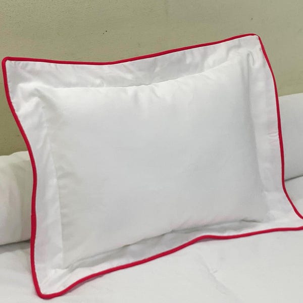 Può includere: Cuscino bianco con bordo rosso. Il cuscino è realizzato in un tessuto morbido e liscio e ha un design semplice ed elegante.