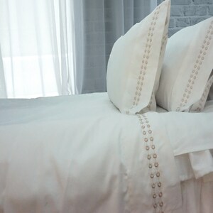 May include: White bedding with a subtle pattern of small circles in a light brown color. The bedding is made of a soft, luxurious fabric and is perfect for a comfortable night's sleep.