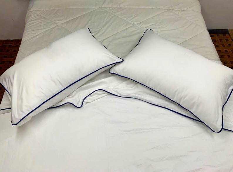 Puede incluir: Dos fundas de almohada blancas con un borde azul oscuro sobre una colcha blanca.