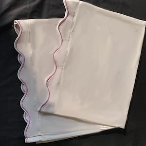 Puede incluir: Dos fundas de almohada blancas con un borde festoneado y un fino ribete rosa.