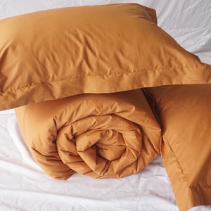 May include: A set of mustard yellow bedding, including a duvet and two pillowcases. The duvet is rolled up and the pillowcases are folded.
