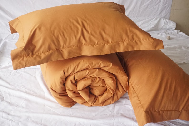 May include: A set of mustard yellow bedding, including a duvet and two pillowcases. The duvet is rolled up and the pillowcases are folded.