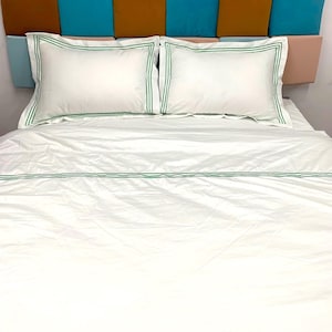 Puede incluir: S&aacute;banas de cama blancas con ribete verde. La cama est&aacute; hecha con una funda n&oacute;rdica blanca y dos fundas de almohada blancas, todas con un fino borde verde.