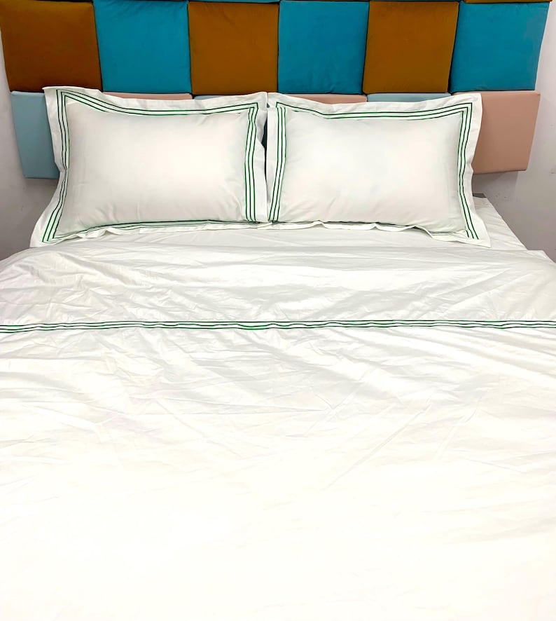 Puede incluir: S&aacute;banas de cama blancas con ribete verde. La cama est&aacute; hecha con una funda n&oacute;rdica blanca y dos fundas de almohada blancas, todas con un fino borde verde.