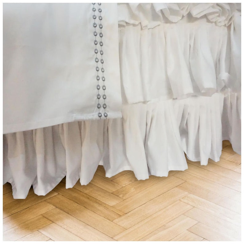 May include: White bed skirt with a ruffled edge and a row of silver beads sewn along the side.