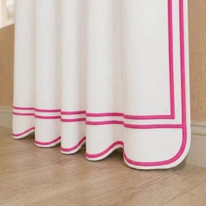 May include: A white curtain panel featuring a double hot pink border trim that follows the bottom and side edges. The fabric hangs in soft, vertical folds, creating a series of rounded, scalloped-like shapes along the lower hemline.