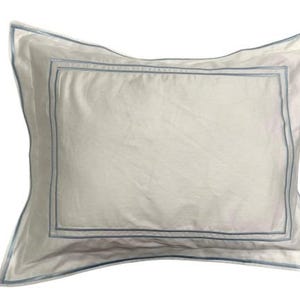 Puede incluir: Una funda de almohada blanca con un doble borde azul.