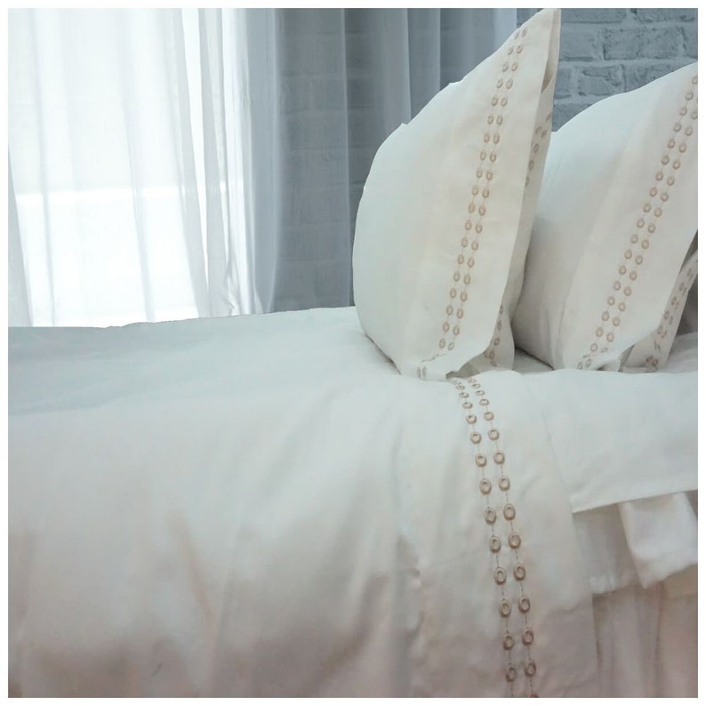 May include: White bedding with a decorative embroidered border of small circles in a light brown color.