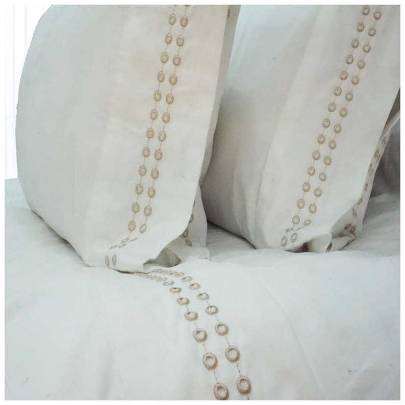 May include: Two white pillowcases with a decorative pattern of brown circles along the edges.