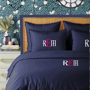 May include: A navy blue duvet cover with a scalloped edge and the monogram "REM" embroidered in pink on the front.
