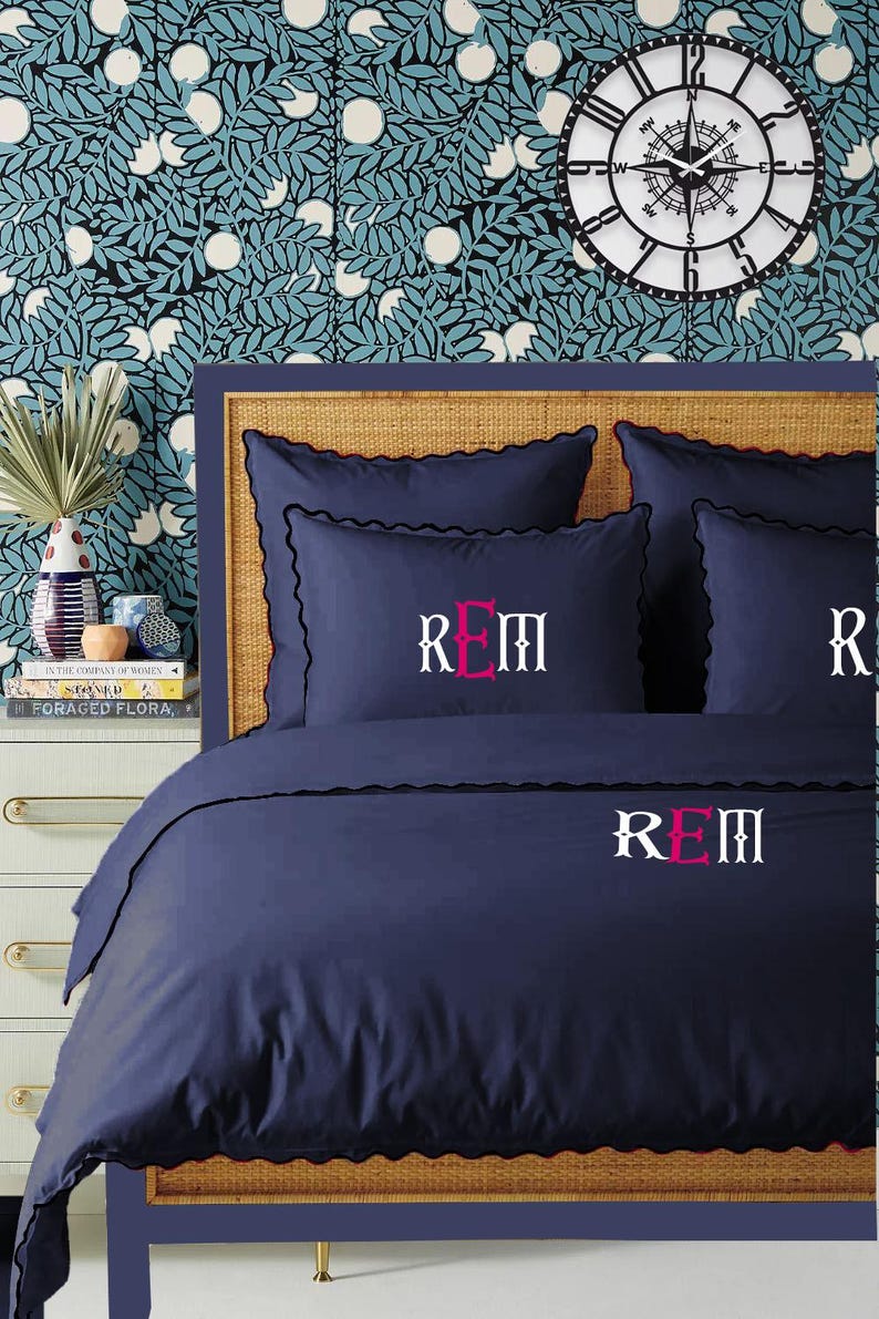 May include: A navy blue duvet cover with a scalloped edge and the monogram "REM" embroidered in pink on the front.