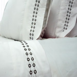 May include: White pillowcases with a decorative pattern of two rows of dark gray circles.