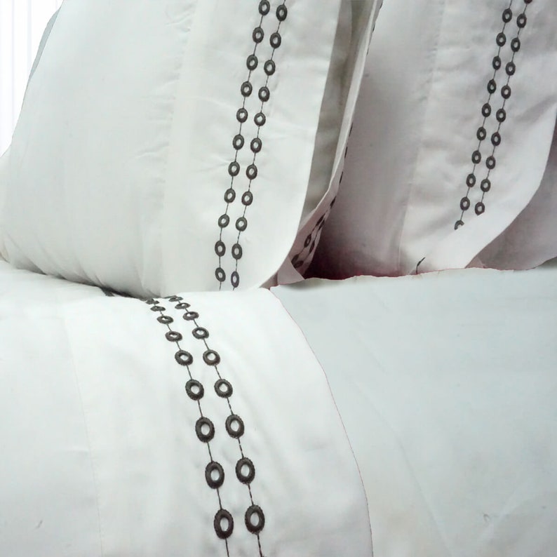 May include: White pillowcases with a decorative pattern of two rows of dark gray circles.