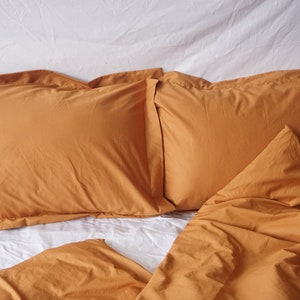 May include: Two mustard yellow pillowcases and a mustard yellow duvet cover on a white bed.