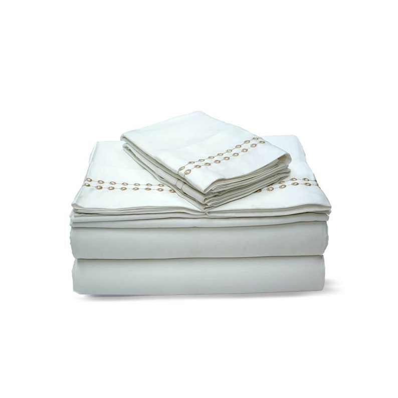 May include: A set of white bed sheets with a brown embroidered pattern. The sheets are folded and stacked on top of each other.
