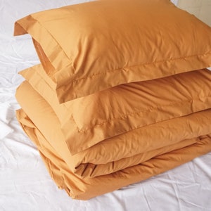 May include: A stack of folded mustard yellow bedding, including a duvet and pillowcases, on a white surface.