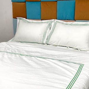Puede incluir: Ropa de cama blanca con ribete verde. La ropa de cama est&aacute; en una cama con una cabecera hecha de cuadrados marrones y azules.