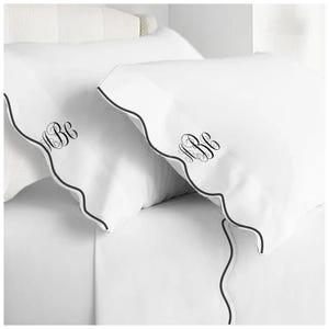 May include: Two white pillowcases with black scalloped edging and the monogram "ABC" embroidered in black script.